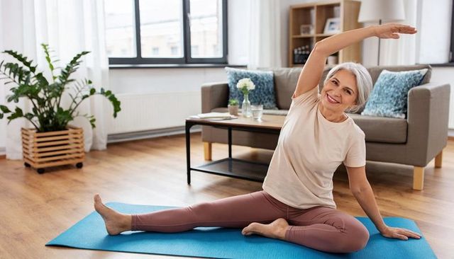 Senior woman practicing seated side stretch on mat in sunlit living room for healthy aging