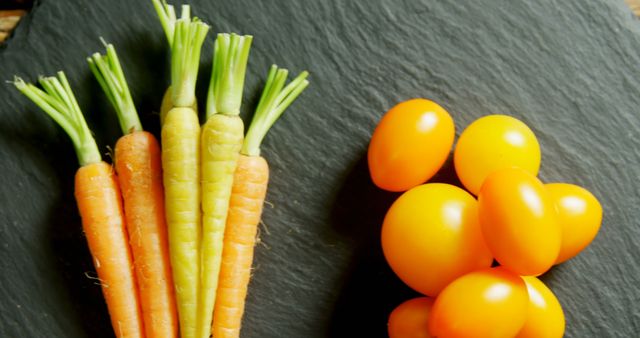 Fresh carrots and cherry tomatoes are arranged on a dark slate surface, showcasing vibrant colors and healthy food choices. Carrots provide essential nutrients while cherry tomatoes add a juicy burst of flavor to any meal.