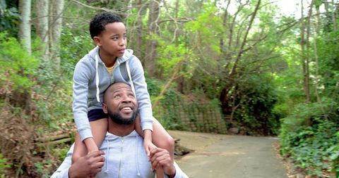 African american father carrying son on shoulders walking forest trail bonding and smiling