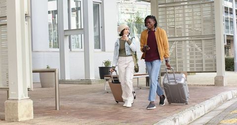 Young diverse travelers walking with suitcases and coffee in urban transit plaza