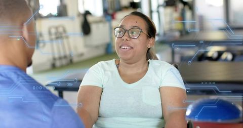 Woman in wheelchair discussing rehabilitation plan with therapist in bright gym