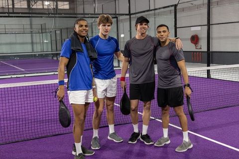 Diverse men posing on purple indoor pickleball court holding paddles and ball, team camaraderie