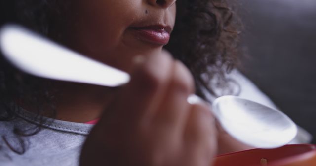 Close-up capturing child with curly hair eating using spoon, showcasing innocence and moment of daily life. Can be used in articles, advertisements, and campaigns highlighting child nutrition, parenting tips, health and wellness related themes, and family moments.