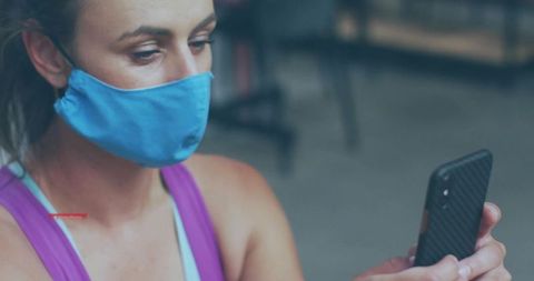 Masked woman in gym checking smartphone for fitness motivation