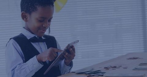 Boy calculating savings on tablet while sorting coins and cash at wooden desk