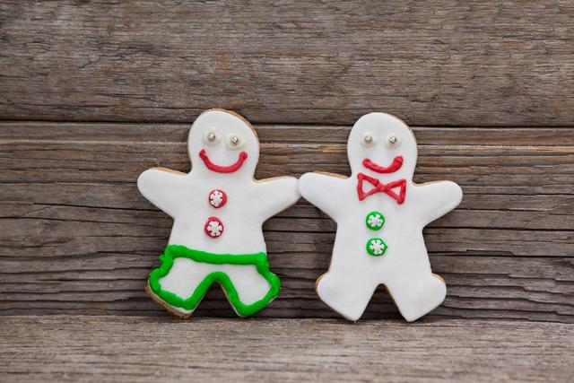 Two gingerbread cookies decorated with colorful icing, leaning against a wooden plank. Ideal for holiday-themed promotions, Christmas cards, festive recipes, and winter celebration advertisements.