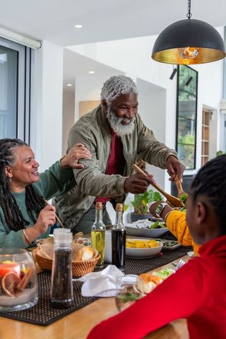 African american family sharing meal in modern kitchen, senior serving salad with tongs
