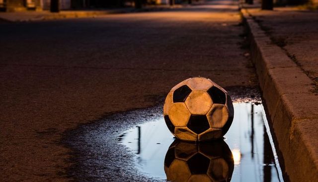 Worn soccer ball reflecting streetlight in puddle on empty urban street at night