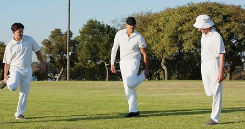 Cricket teammates stretching on sunlit oval before match, team warmup and training
