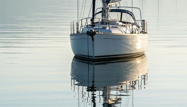 Sailboat floating on glassy water creating near-perfect reflection with anchor chain