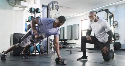 Trainer Guiding Client in Dumbbell Renegade Row at Gym