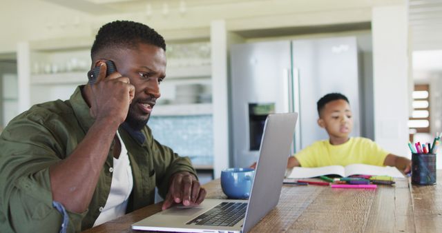 Young boy studying next to his father who is working on a laptop and talking on the phone. This can be used to illustrate remote work, parenthood, education, and work-life balance. Perfect for articles about modern families, home education, and multitasking parents.