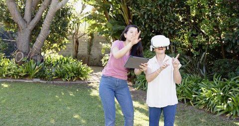Asian senior woman exploring vr headset while daughter guiding with tablet in garden