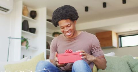 Happy man opening red gift box at home during cozy relaxation time