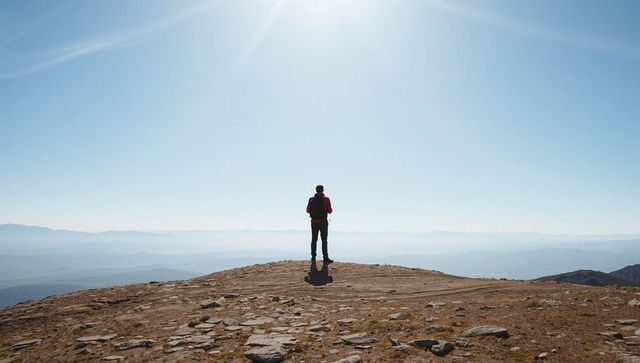 Solo hiker standing on mountain summit overlooking vast alpine panorama and horizon view