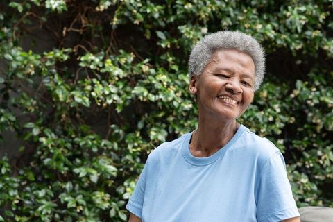 Senior african american woman smiling and standing in garden wearing light blue tee