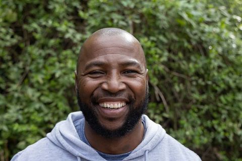 Smiling african american man wearing gray hoodie outdoor headshot with beard and greenery