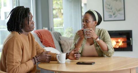 African American Couple Sharing Coffee and Conversation at Cozy Home Table by Fireplace
