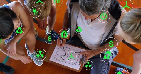 Youth basketball coach drawing strategy on clipboard on court with green tech icons