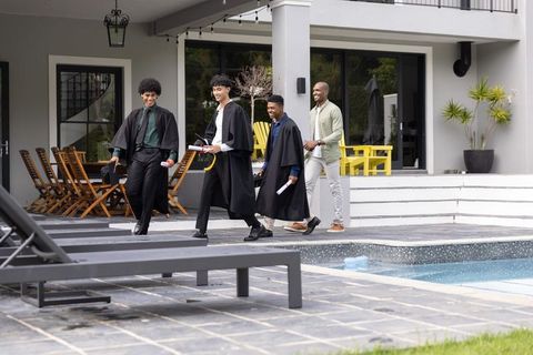 Young graduates walking poolside at modern home celebrating achievement with diplomas