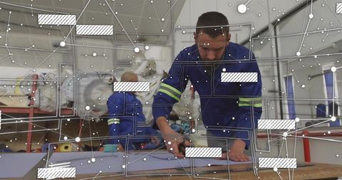 Textile worker cutting foam on workbench in hi-vis coveralls with digital network overlay