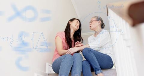 Young woman holding hands with older woman on stairs sharing comfort and math tutoring