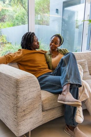 African american couple relaxing on sofa in modern living room with garden view