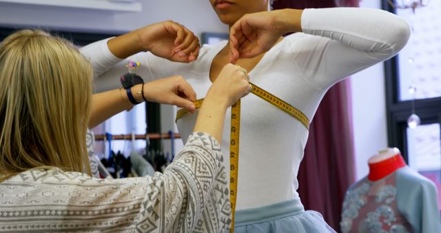 A Caucasian tailor is measuring the arm of a young Caucasian ballerina, with copy space. Precision is key in customizing dance costumes to ensure a perfect fit and elegant performance.