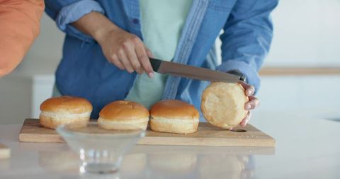 Slicing sandwich buns on wooden board in bright kitchen preparing homemade burgers