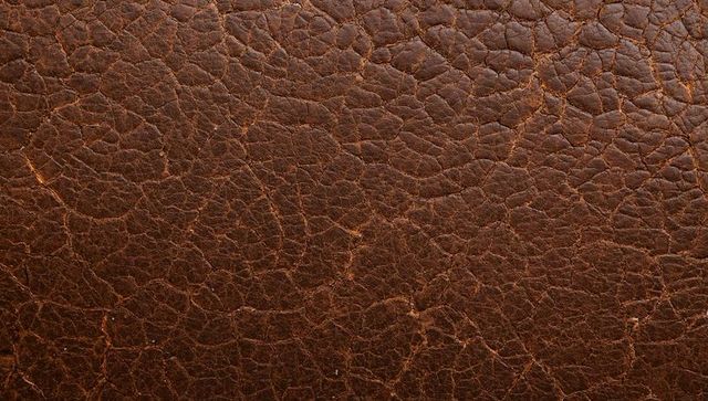Macro brown leather texture showing cracked grain, worn patina and distressed scuffs