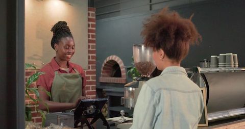 Smiling barista operating pos tablet at coffee counter with espresso machine, brick arch