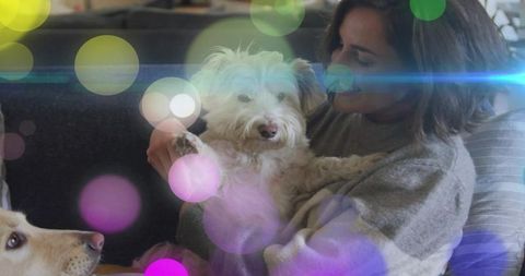 Woman cradling small white fluffy dog on couch with warm bokeh lights, cozy pet moment