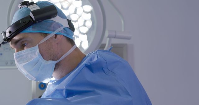 Front view of a Caucasian male surgeon at work in a hospital operating theatre wearing a surgical cap, mask, gown and a head lamp, selecting tools for the operation