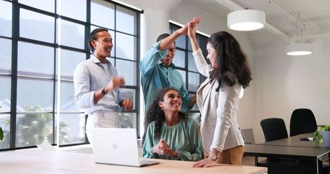 Diverse office team celebrating success around laptop