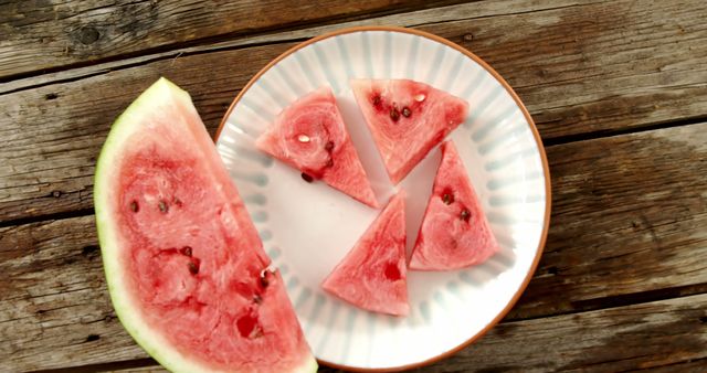 Slices of ripe watermelon are arranged on a plate on a rustic wooden table, with copy space. Watermelon, a refreshing summer fruit, is often enjoyed for its sweet and hydrating qualities.
