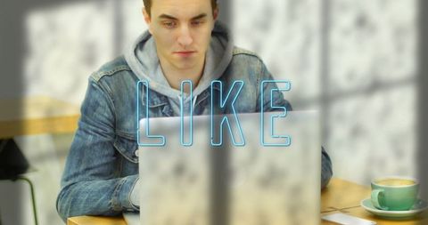 Young Man in Denim Jacket Working on Laptop at Cafe with LIKE Graphic