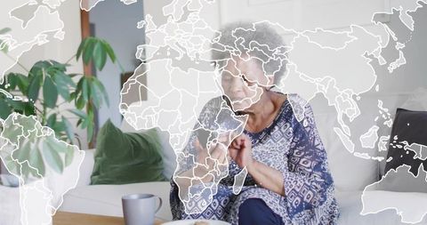 Senior woman inspecting fingertips on sofa with world map overlay, wellness mindfulness