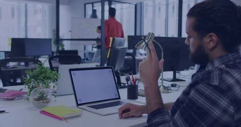 Bearded man reaching and adjusting brass desk lamp while working at modern open-plan office