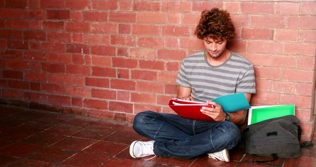 Student sitting against wall reading textbook at the university