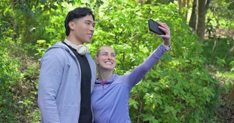 Young couple capturing selfie on sunlit forest trail during casual outdoor hike