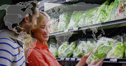 Couple in supermarket choosing fresh lettuce with world map overlay