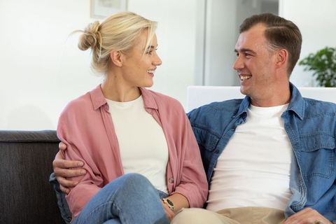 Couple sitting close on sofa smiling and holding each other in bright modern living room