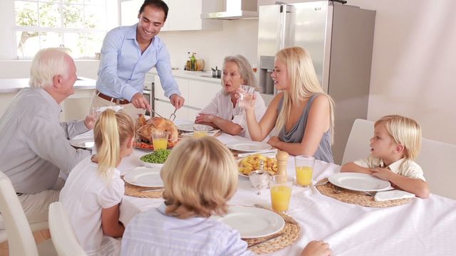 This cozy scene captures a family gathering for a holiday dinner, with a father carving a turkey while surrounded by his family at a table. Perfect for use in promoting family-friendly products or services, advertisements celebrating holidays and festive events, or blog posts about family traditions and holiday celebrations.