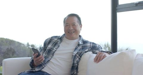 Senior Man Smiling while Holding Smartphone in Bright Living Room