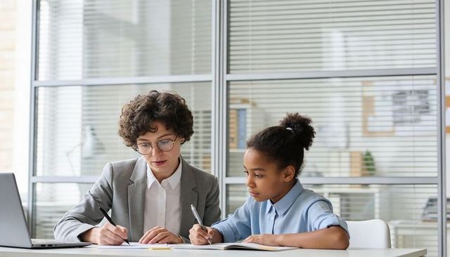 Teacher mentoring student at desk studying together with laptop and notebooks