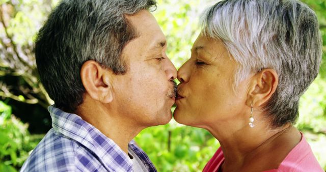 A middle-aged Asian couple shares a tender kiss outdoors, with copy space. Their affectionate moment captures a sense of enduring love and companionship.