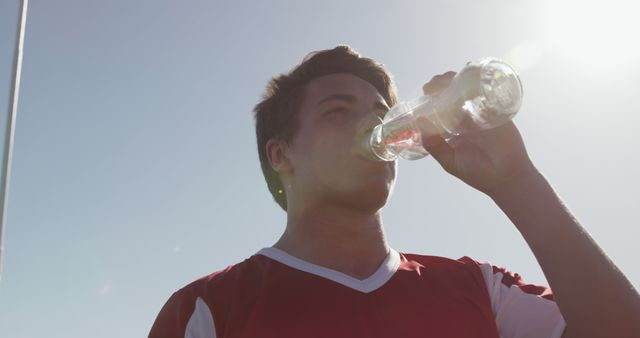 Young athlete hydrating with water under bright sunlight. Suitable for promoting sports events, health hydration tips, and showing the importance of staying hydrated during physical activities.