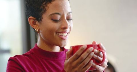 Cozy morning ritual woman holding red mug smiling closeup warm beverage natural light