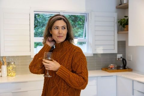 Cozy autumn woman wearing burnt-orange cable-knit sweater holding wine glass in modern kitchen