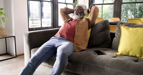 Senior man relaxing on sofa with headphones in modern living room